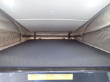 Inside an RV rental pop-top, showing the elevated sleeping area with a patterned mattress & fabric sides.