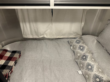 Cozy RV rental bed features light gray linens, a red plaid blanket, and patterned pillows. Perfect for a comfortable travel trailer trip.