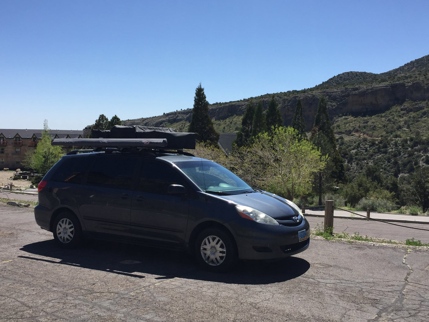 Dark gray Toyota Sienna minivan with roof-mounted gear for travel, parked near a lodge in mountains. Perfect for an rv rental adventure.