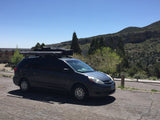 Dark gray Toyota Sienna minivan with roof-mounted gear for travel, parked near a lodge in mountains. Perfect for an rv rental adventure.