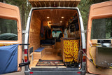 An RV rental's warm, custom wood interior with a bed, kitchen, and unique outdoor water heater visible from the back.