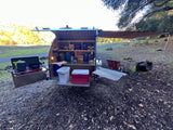 This RV rental teardrop trailer displays its organized galley kitchen, stove, cooler, and side awning for camping comfort.