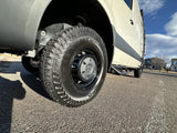 Up close of an RV rental's front wheel, showcasing the rugged Kumho Road Venture AT tire and side step of a cream-colored van.