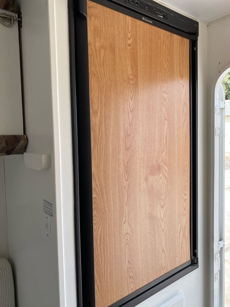 Clean RV rental interior featuring a Dometic refrigerator with a wood-grain panel, adjacent to a white wall with controls.