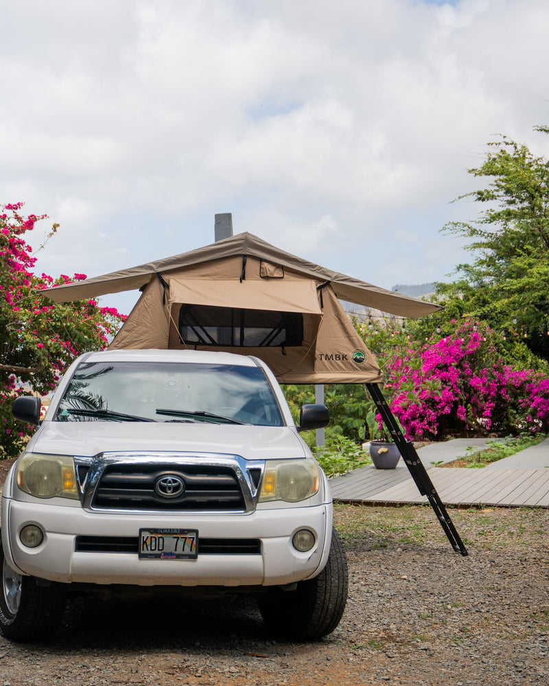 White Toyota Tacoma with a tan rooftop tent and ladder, an ideal RV rental for outdoor adventures amidst lush greenery. — photo 13