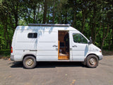 White camper van for rv rental parked in forest with open side door revealing custom interior. Perfect for van life adventures!