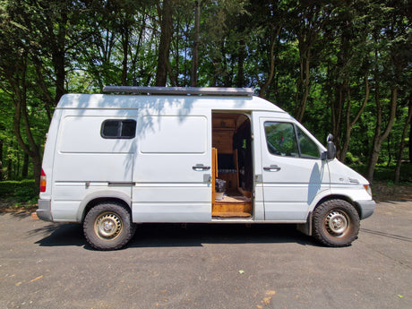 White camper van for rv rental parked in forest with open side door revealing custom interior. Perfect for van life adventures!