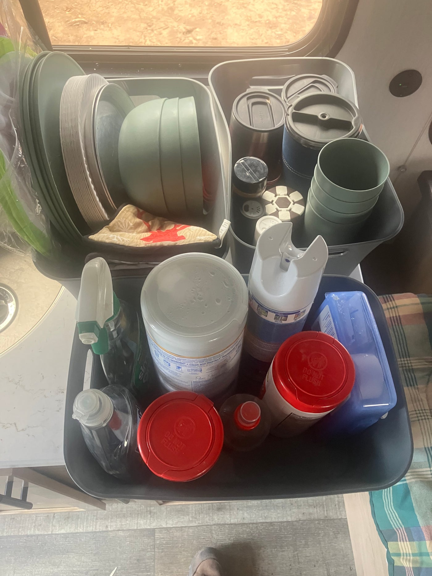 An RV rental's organized storage bins hold kitchen plates, bowls, cups, and various cleaning supplies like sprays and wipes. — photo 5
