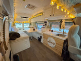 Cozy RV rental interior with winter decor, string lights, and fake snow, featuring a dinette, kitchen sink, and snowy views.