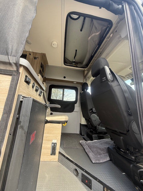 This RV rental offers a cozy interior: swiveling front seats, compact storage, a control panel, and a ceiling vent.