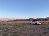 White campervan RV rental at a serene desert campsite, framed by majestic mountains. Ideal for scenic van life adventures.