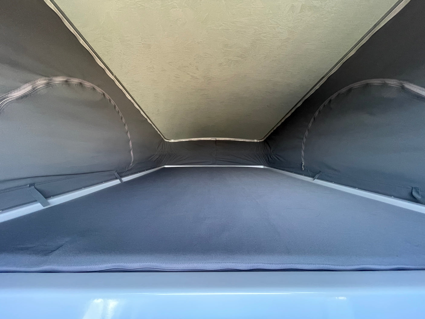 RV rental pop-top: Interior view of the bed area with grey fabric walls and a light, textured roof above.