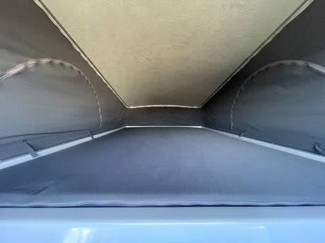 RV rental pop-top: Interior view of the bed area with grey fabric walls and a light, textured roof above.