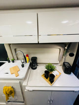 Modern RV rental kitchen shows sink, coffee maker, toaster, and stylish decor on white countertops.
