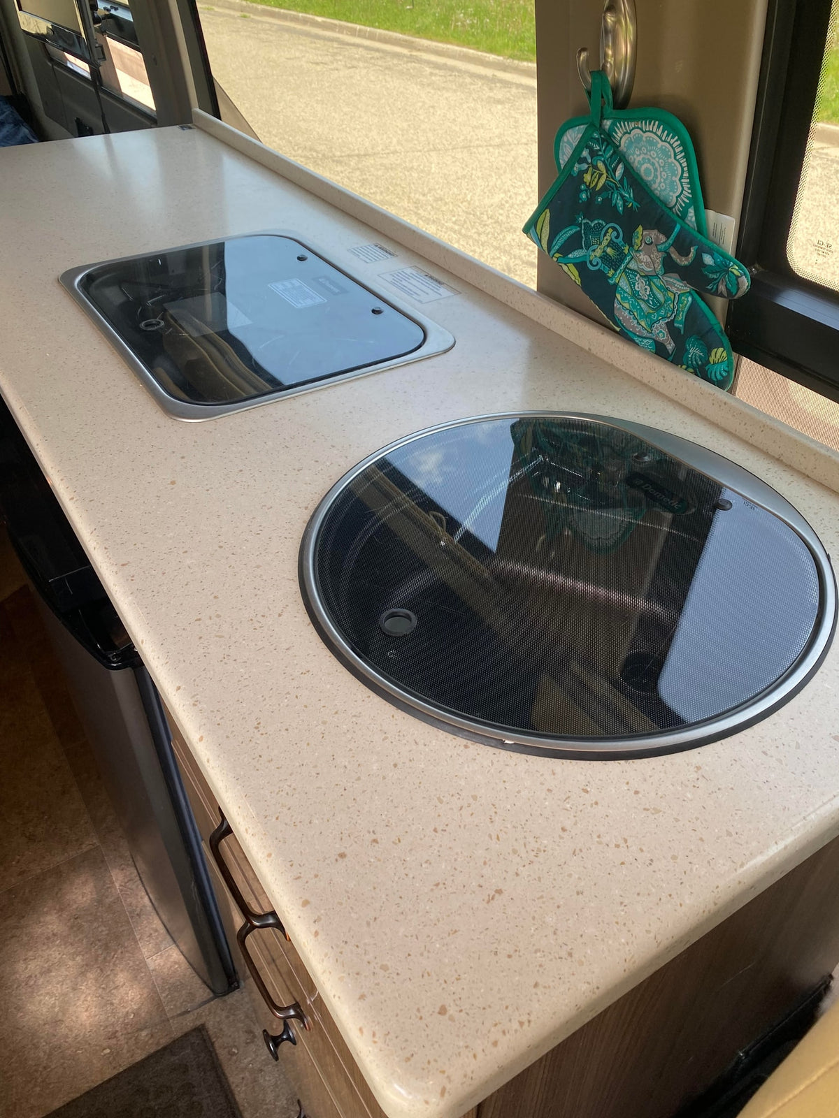 This **RV rental** kitchen features a compact countertop with a sleek built-in cooktop and sink. Oven mitts hang nearby. — photo 6