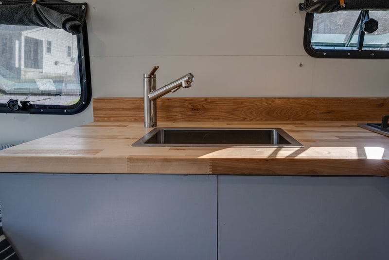 Bright RV rental kitchen with modern stainless steel sink, faucet, and warm wood countertops. — photo 18