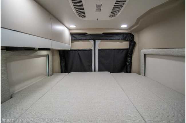 View inside an rv rental camper van: light-colored interior with a large bed, overhead cabinets, and rear privacy covers.