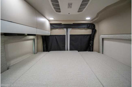 View inside an rv rental camper van: light-colored interior with a large bed, overhead cabinets, and rear privacy covers.
