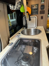 RV rental kitchen featuring a compact sink, stove, and comprehensive utility control panel with generator and water functions.