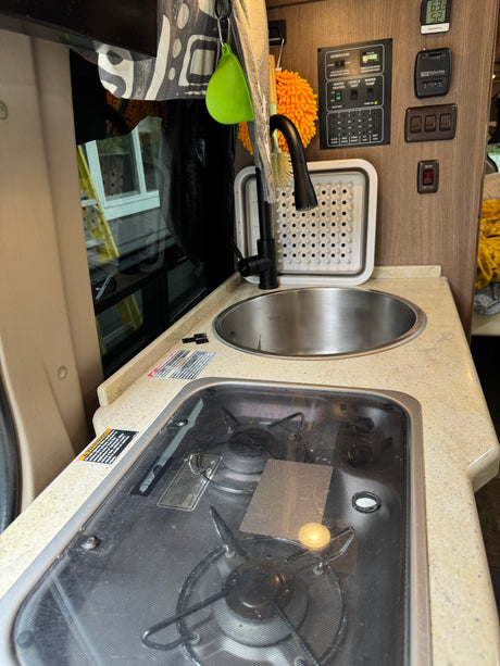 RV rental kitchen featuring a compact sink, stove, and comprehensive utility control panel with generator and water functions.
