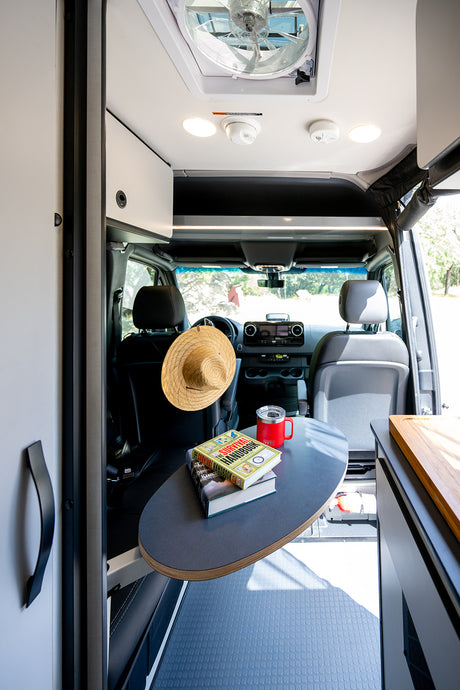 Cozy rv rental interior featuring a flexible table with books and mug, plus a ceiling fan for comfort.