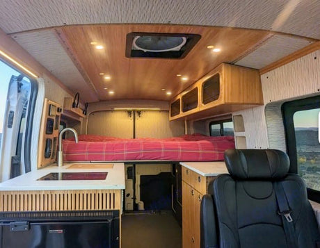 This inviting RV rental offers a well-designed camper van interior with a comfy bed, functional kitchen, and warm wood details.