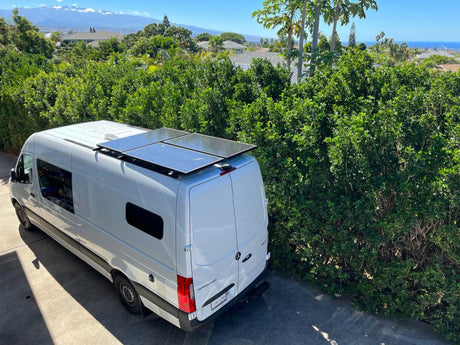White Sprinter camper van RV rental with rooftop solar panels, ready for adventures in a scenic, lush setting.