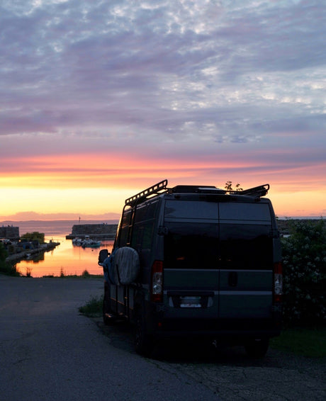 Vibrant sunset over a harbor with an RV rental camper van parked nearby. Perfect for scenic road trips.