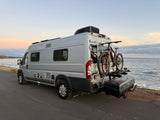 Grey camper van RV rental parked by the ocean with bikes on the rear rack. Enjoying a coastal sunset adventure.