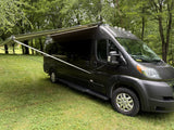 Dark gray campervan with an extended awning parked on green grass amidst trees, perfect for an RV rental getaway.