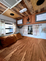 Warm & inviting RV rental bedroom with textured orange bedding, patterned curtains, and rustic wood ceiling.