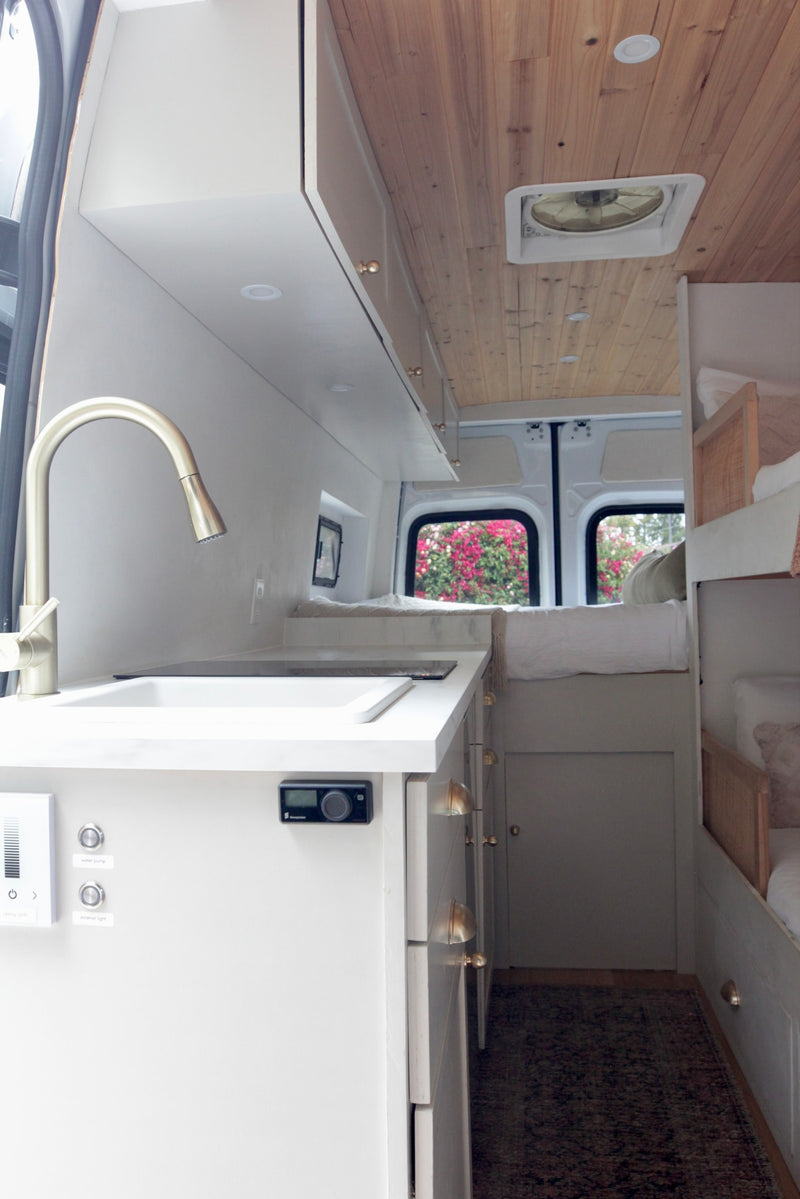 Step inside this modern RV rental: a compact interior with a kitchen counter, sink, and faucet, plus cozy bunk beds on the right. Wood ceiling. — photo 6