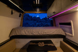 Step into this modern **rv rental**'s cozy interior, featuring a comfortable bed and a window framing a moonlit rocky landscape.