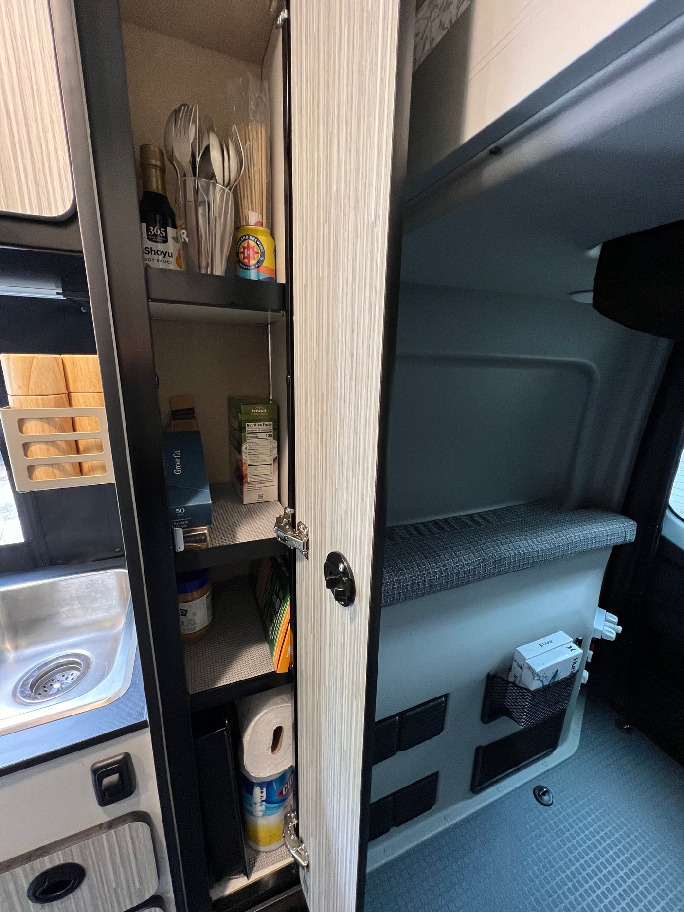RV rental kitchenette features an open pantry with food, utensils, cleaning supplies, a sink, and integrated bench storage.