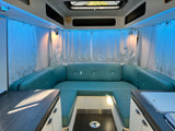 Interior of an rv rental: U-shaped turquoise dinette, ambient blue lighting, overhead storage, and counters. A modern camper layout.