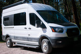 White Ford Transit camper van RV rental, custom-built for adventure, parked on a forest road.