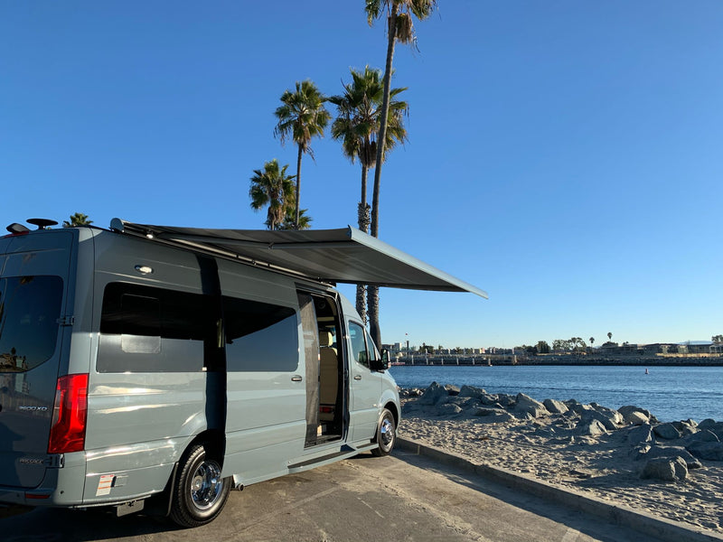  parked by a sunny bay with palm trees. Adventure awaits!|An RV rental van is parked on a scenic road — photo 2