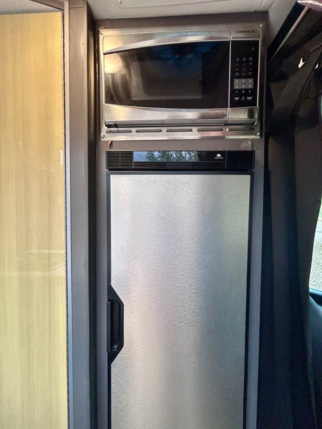 This RV rental features stainless steel kitchen appliances: a microwave mounted above a matching refrigerator.