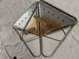 Durable Snow Peak folding metal camp stove, visibly used, ideal for RV rental outdoor cooking. On a light grey fabric surface.