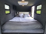 RV rental interior: Cozy camper bed with storage, TV, and windows.