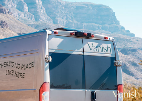 A Vanish RV rental van, featuring custom text, sits parked against a stunning backdrop of rugged desert mountains.
