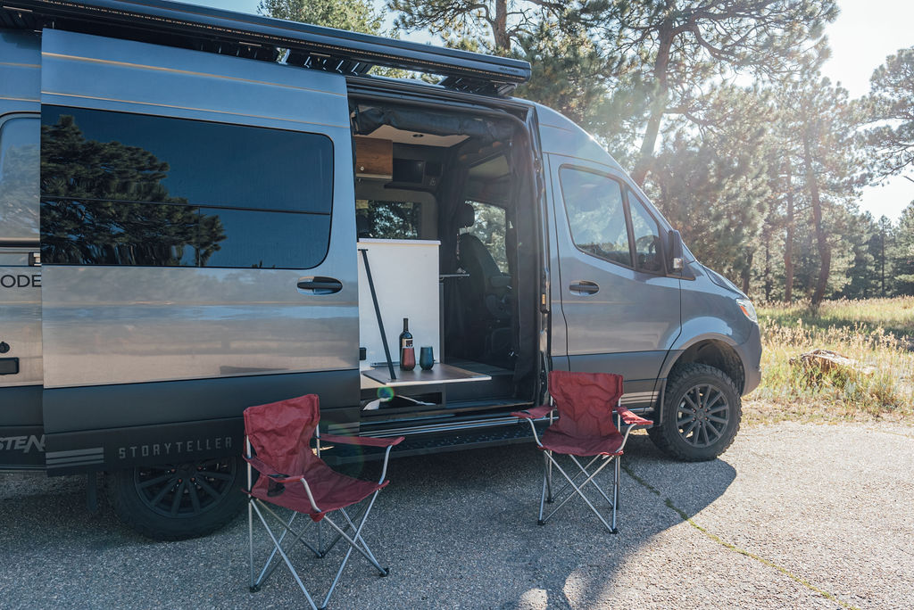  backed by majestic mountains and a lush forest.|Grey Storyteller Overland camper van with side door open — photo 2