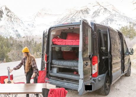Ready for adventure? Our RV rental camper van, shown here with a woman and guitar, features bunk beds in a mountain setting.
