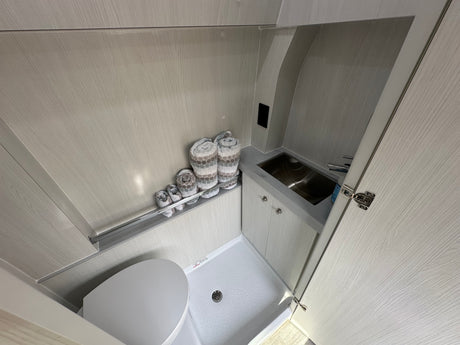 This RV rental features a compact wet bath with a toilet, shower base, stainless steel sink, and light wood-textured interior.