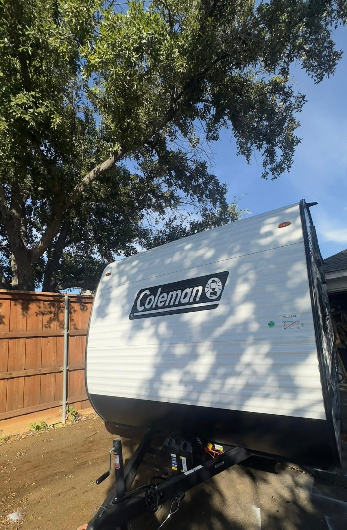 A white Coleman travel trailer parked outdoors under a sunny sky, with tree shadows. Perfect for your next RV rental adventure. — photo 11