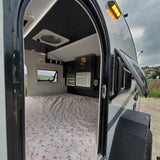 View of a compact rv rental interior with a floral-patterned bed, AC, and overhead cabinets, ideal for travel.