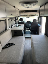 Modern rv rental interior with kitchenette, gray fabric seating, overhead cabinets, and front cab view. Sleek, organized space.