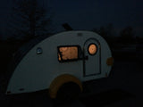 Teardrop rv rental glowing at night. Interior lights show a cozy space, perfect for an adventure.
