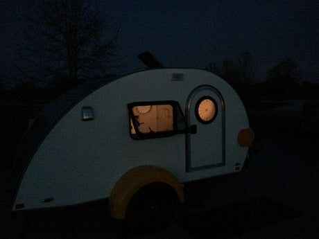 Teardrop rv rental glowing at night. Interior lights show a cozy space, perfect for an adventure.