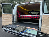 This cozy RV rental camper van features a warm plaid bed, string lights, and a pull-out kitchen for outdoor cooking.